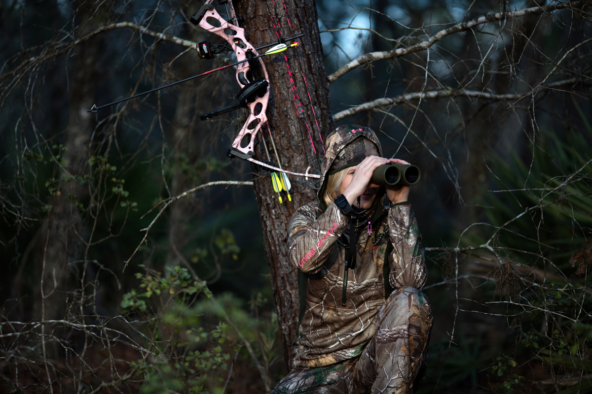 Danielle Harris-Medlock using binoculars in wooded terrain with archery equipment nearby